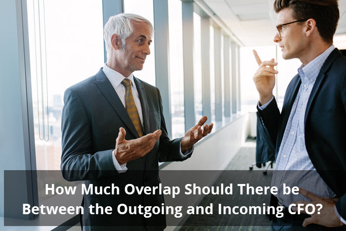 Two executives in discussion in an office corridor beneath the question How Much Overlap Should There be Between the Outgoing and Incoming CFO?