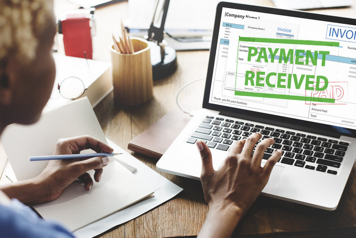 Colleagues at a laptop showing a Payment Received confirmation on an invoice.