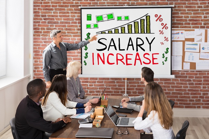 A manager presenting a salary increase chart to employees in a meeting room.