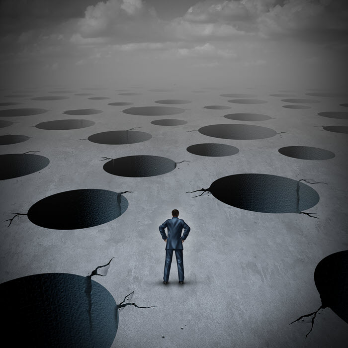 A lone businessman standing among a field of holes in the ground.