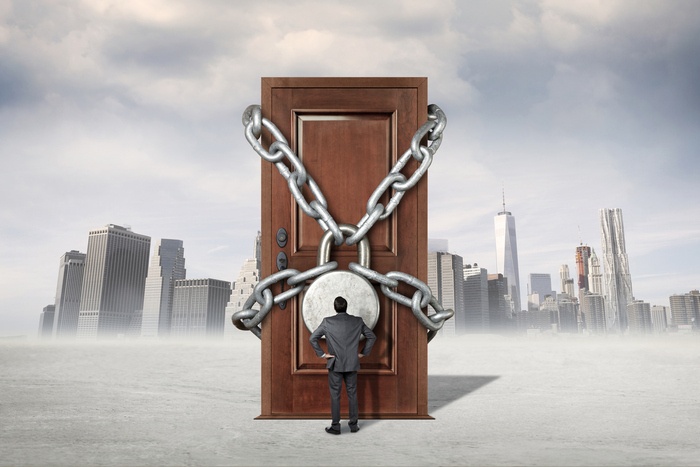 A person standing before a chained and padlocked door set against a city skyline.