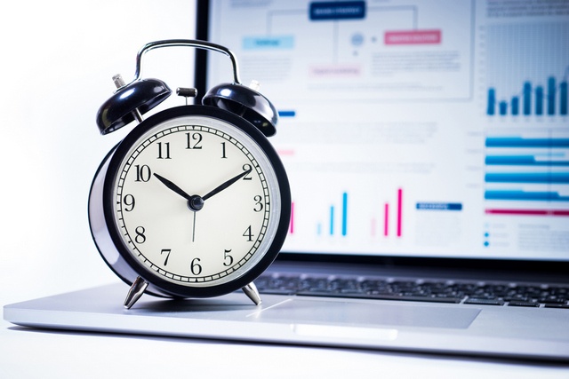 An alarm clock resting on a laptop displaying financial dashboards.