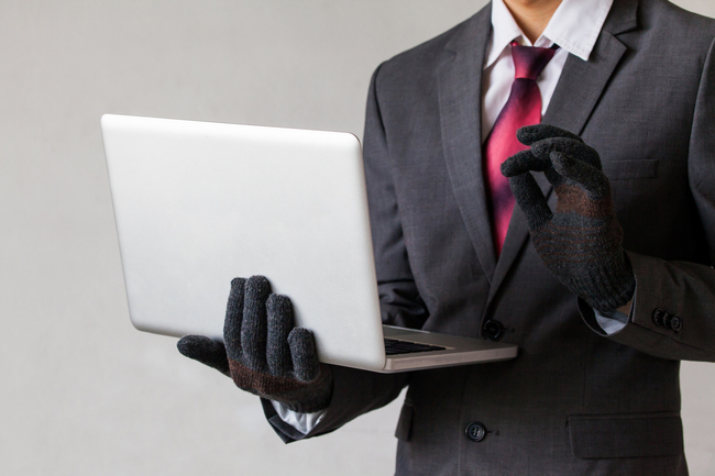 A man in a suit and black gloves holding an open laptop, suggesting email fraud.