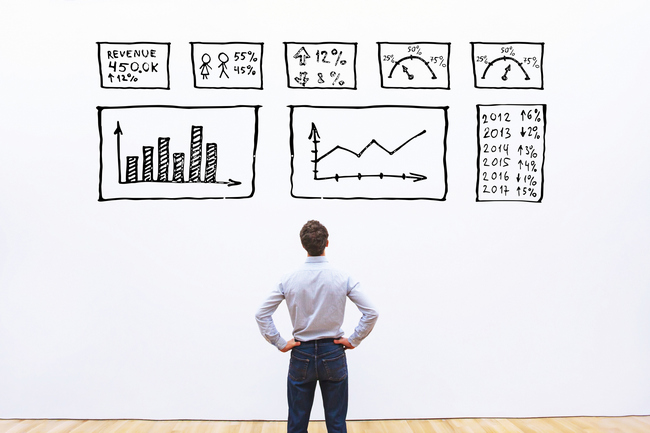 A man standing before a wall of hand-drawn charts and performance metrics.