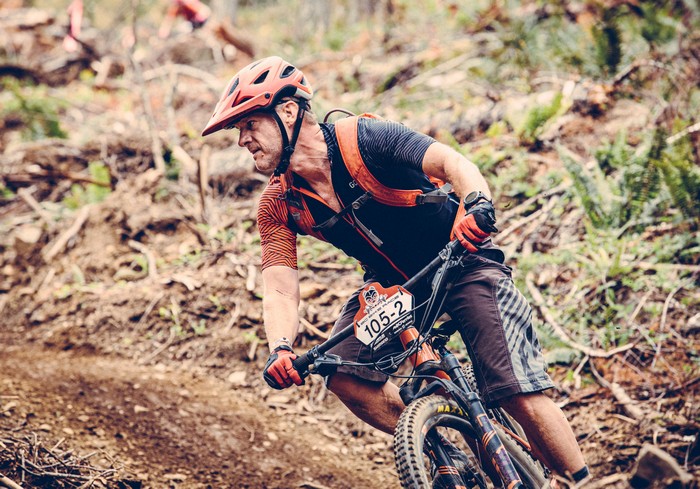 A mountain biker in a helmet riding hard through a dirt corner during a race.