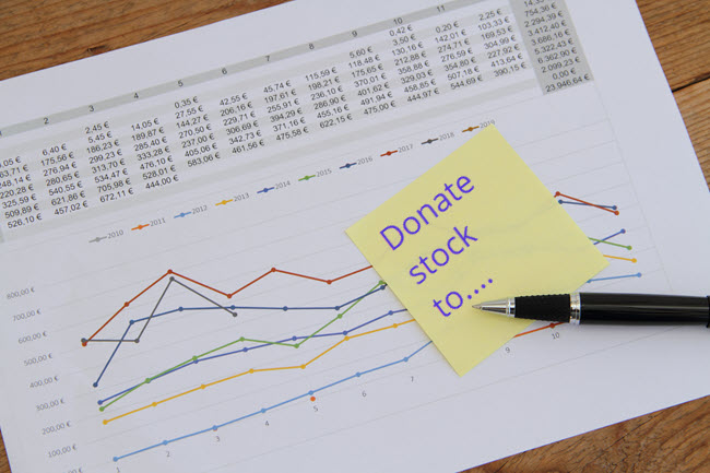 A sticky note reading Donate stock to resting on printed financial charts.