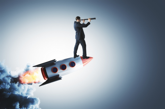 A businessman standing on a launching rocket looking ahead through a telescope.