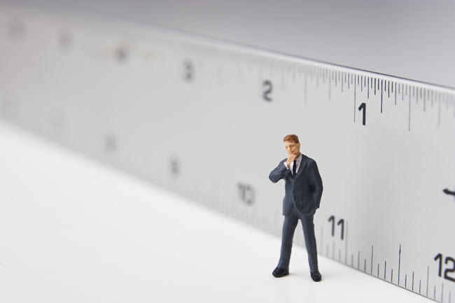 A miniature businessman standing on a ruler, suggesting measurement and fit.