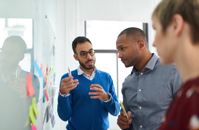 Three colleagues discussing ideas in front of a whiteboard covered in sticky notes.