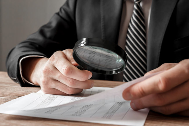 A man in a suit examining a document with a magnifying glass.
