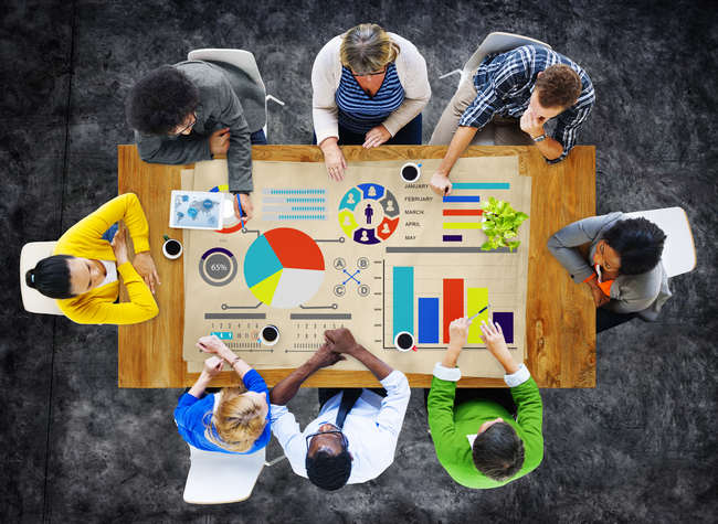 Overhead view of a team collaborating around a table covered in charts and graphs.