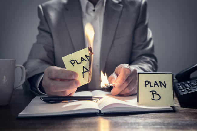 A businessman burning a note marked Plan A while holding one marked Plan B.