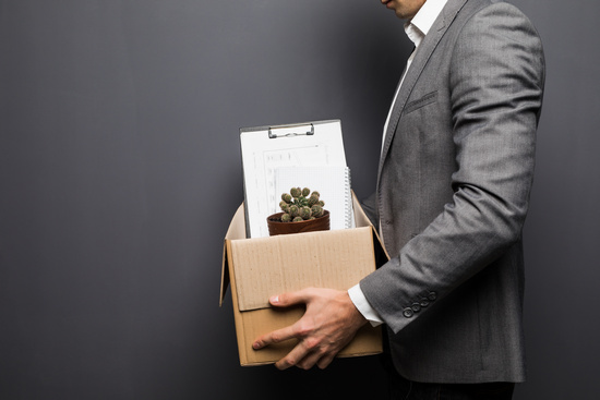 A man in a suit carrying a cardboard box of desk belongings after leaving a job.