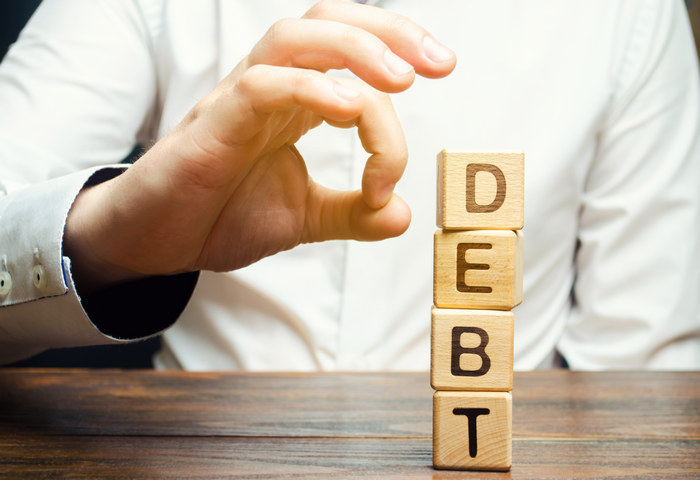 A hand stacking wooden blocks that spell the word Debt.