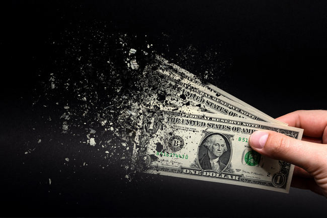A hand holding dollar bills that are dissolving into particles.