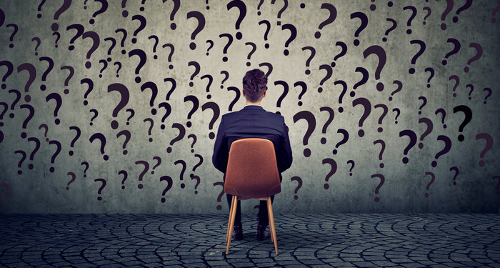 A person sitting alone facing a wall covered in question marks.