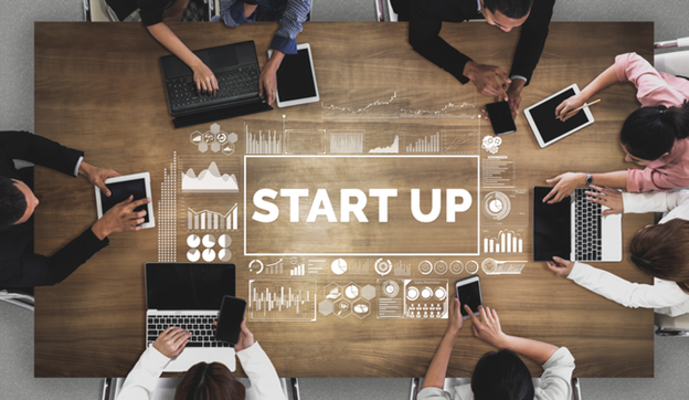 Overhead view of a team working around a table with startup icons and charts overlaid.