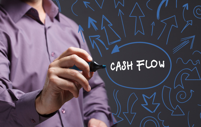 A person writing the words Cash Flow on a chalkboard surrounded by drawn arrows.