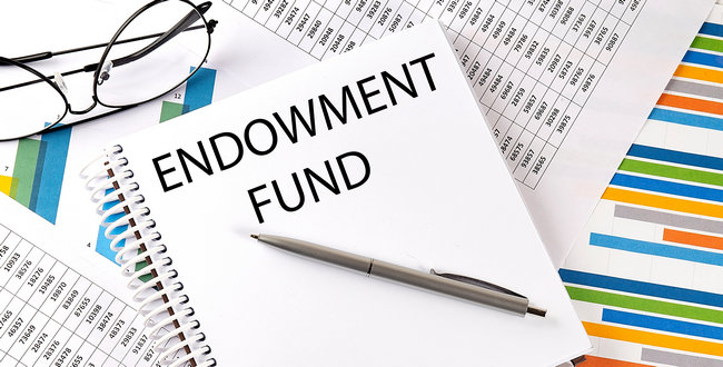 A notepad labeled Endowment Fund resting on financial charts beside glasses and a pen.