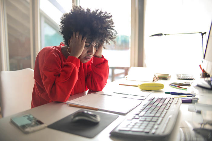 A frustrated worker holding her head in her hands at a desk.