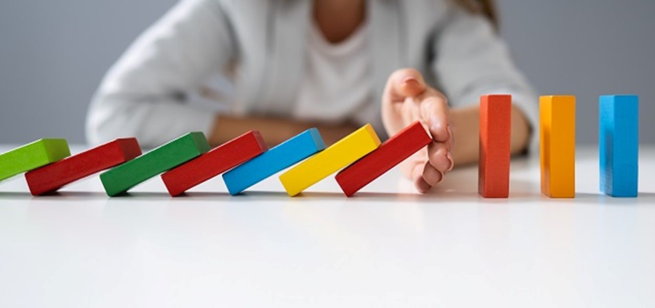 A hand halting a line of toppling colored blocks before they reach the rest.