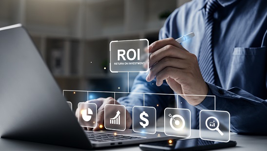 A person at a laptop touching a glowing ROI icon among financial symbols.