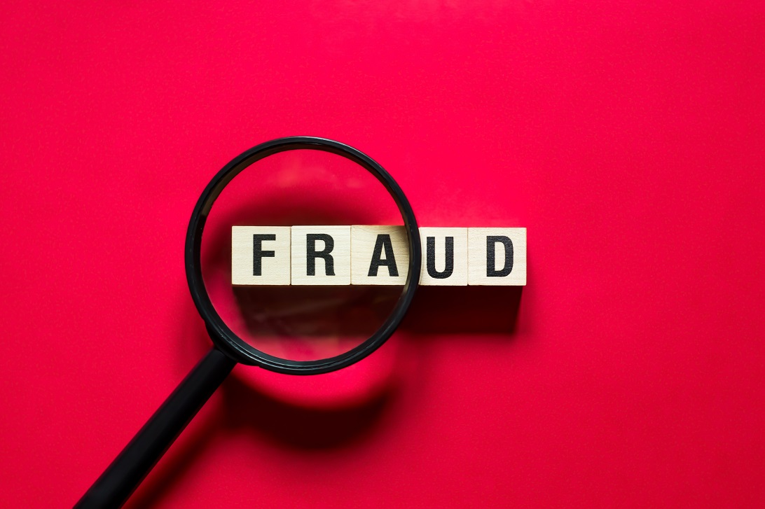 A magnifying glass held over wooden blocks spelling Fraud on a red background.