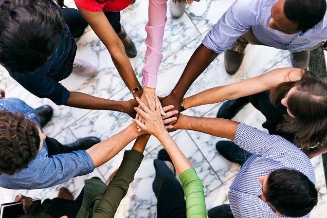 Overhead view of a diverse team stacking their hands together in the center of a circle.