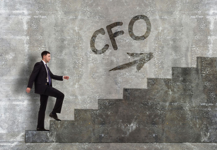 A businessman climbing concrete stairs toward the letters CFO on the wall.