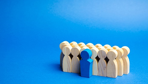 Wooden figures arranged in a group with one blue figure standing out in front.