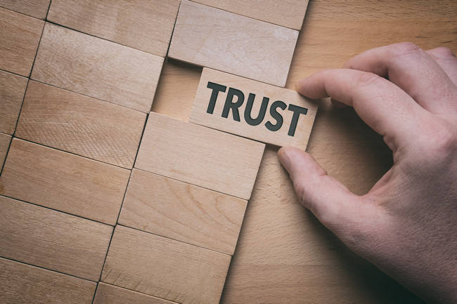 A hand placing a wooden block reading Trust into a row of blocks.