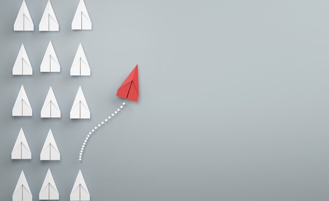 Rows of white paper planes with one red plane breaking away in a new direction.