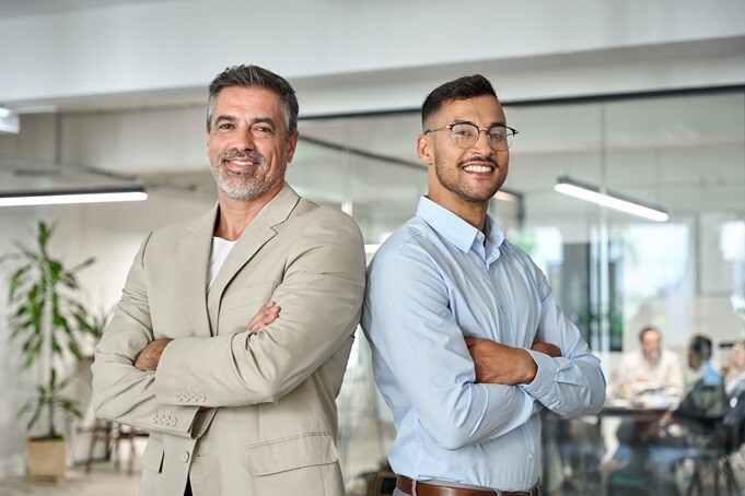Two colleagues standing with arms crossed in a modern open office.