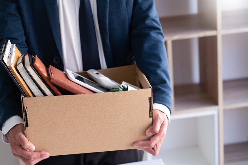 A man in a suit carrying a cardboard box of files and desk belongings out of an office.