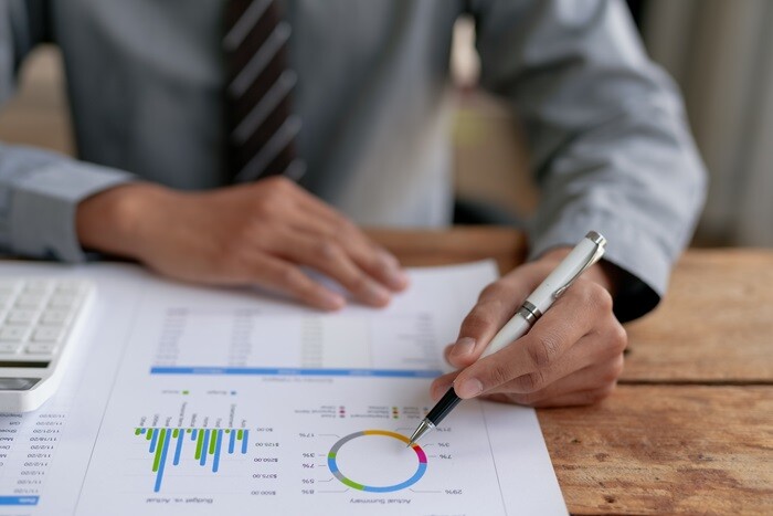 A person marking up printed financial charts with a pen beside a calculator.