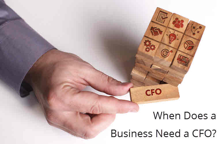 Hands stacking wooden blocks marked with business icons, one labeled CFO, beside the question When Does a Business Need a CFO?