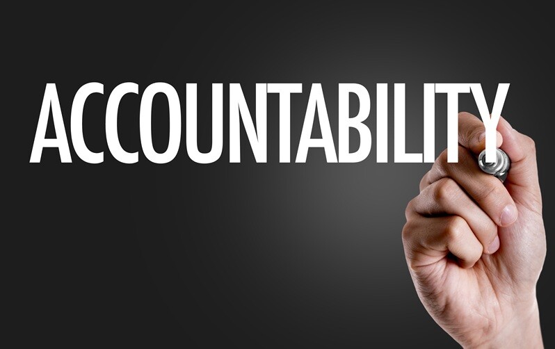 A hand writing the word Accountability on a dark background.