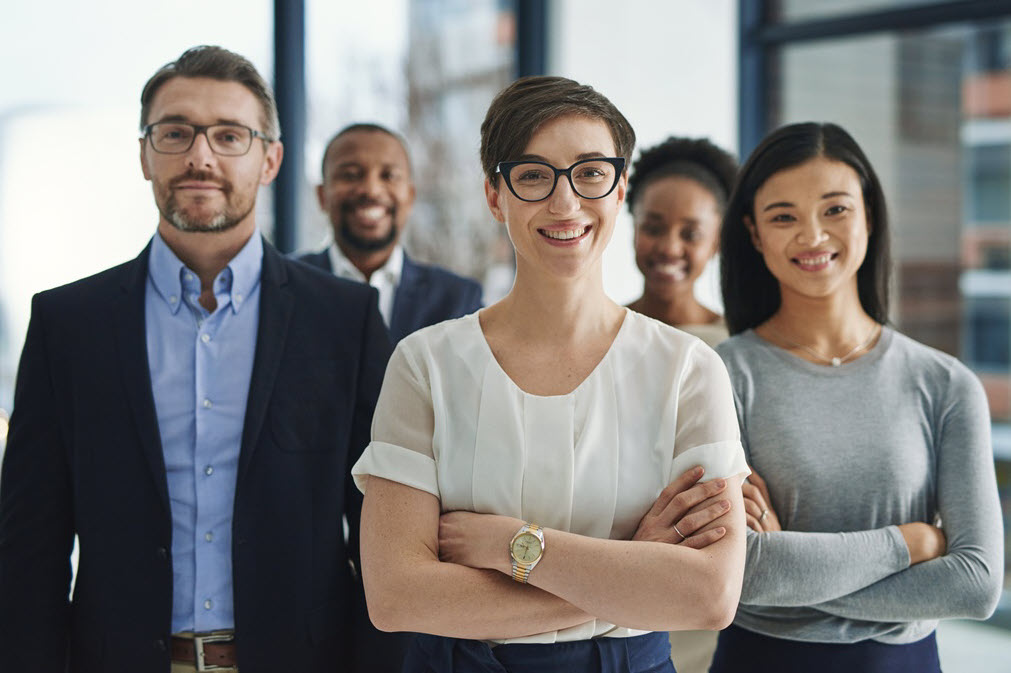 A confident team of five colleagues standing together with arms crossed in an office.