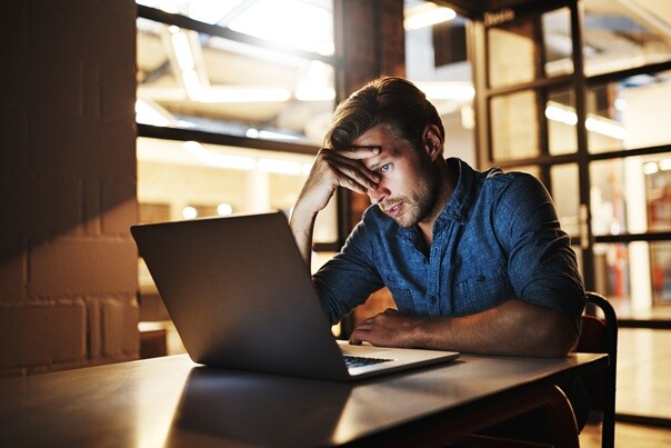 A worried man staring at his laptop in a dimly lit room.