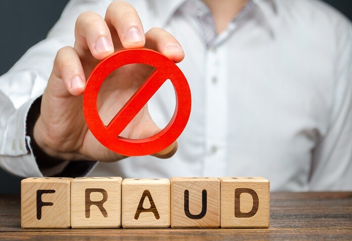 A hand holding a red prohibition sign over wooden blocks spelling Fraud.