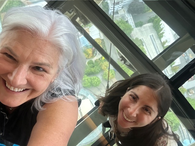 Two women smiling in a selfie inside a glass-walled atrium.
