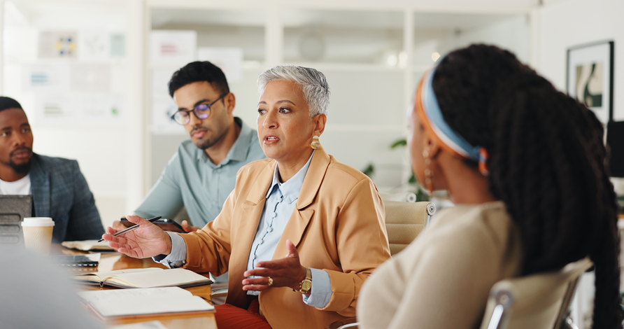 A woman leading a discussion with colleagues around a conference table.