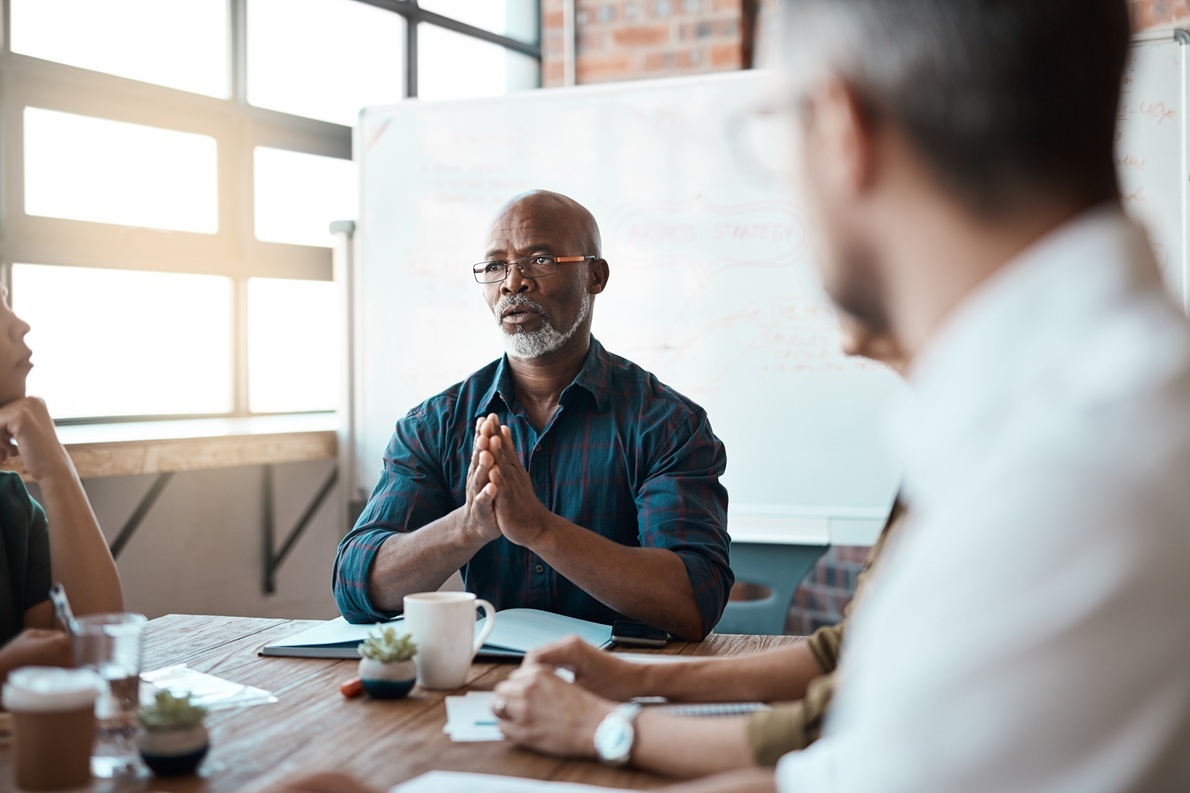 A man leading a discussion with colleagues around a conference table.