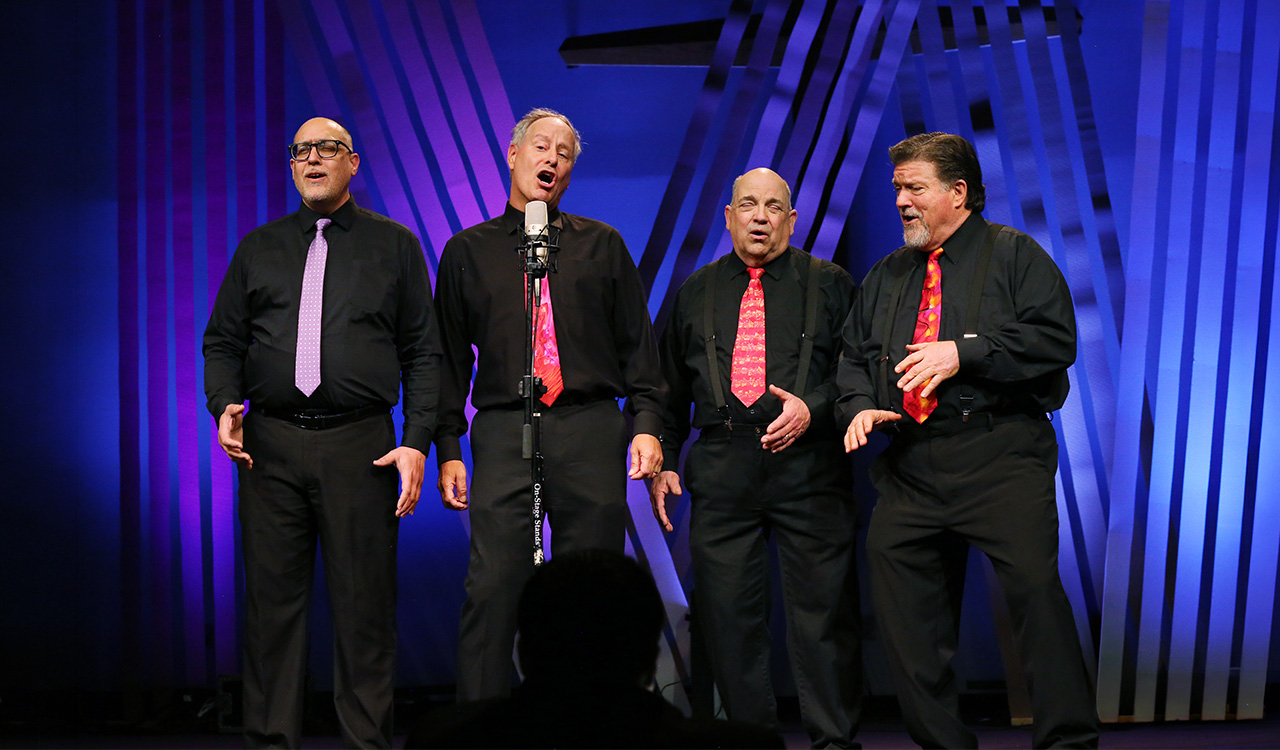 The Firecrest Four quartet performing on stage under blue and purple lighting.