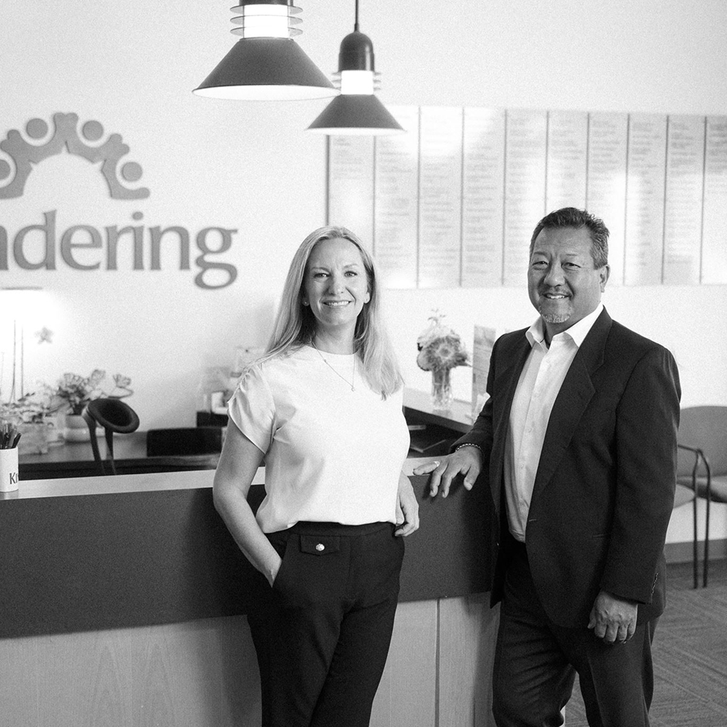 Becky Todd of CFO Selections and Gary Yamamoto standing in front of the Kindering sign at reception.