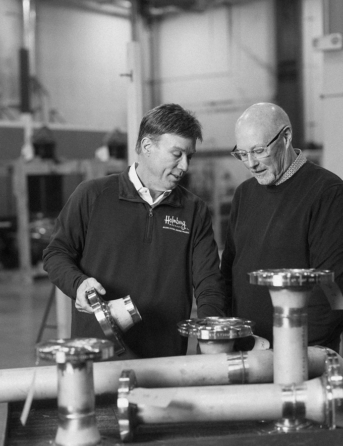Kevin Briscoe of CFO Selections and Jeff White of Holmberg Mechanical examining a pipe fitting on the shop floor.