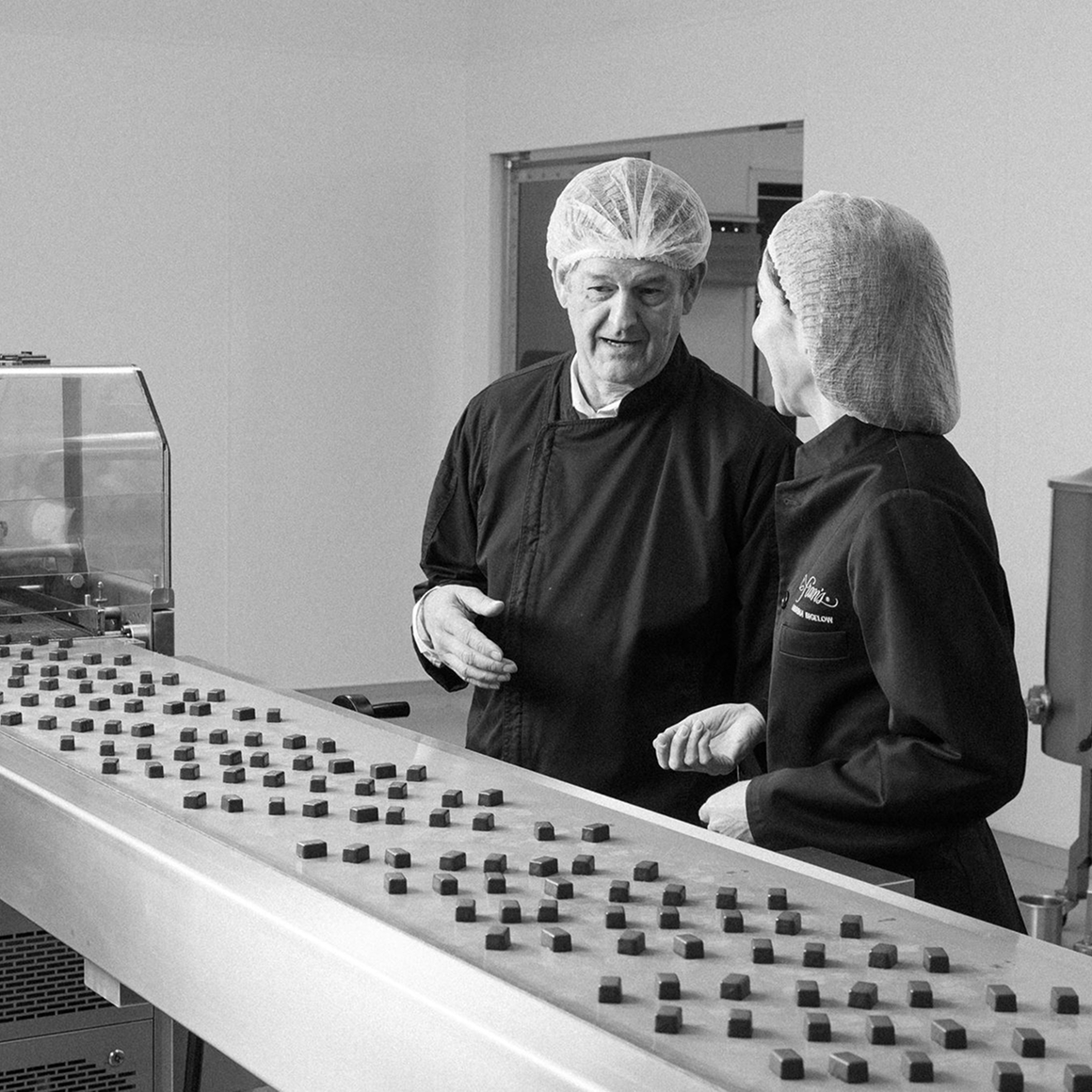 Kurt Maass of CFO Selections and Andrina Bigelow of Fran's Chocolates beside a conveyor of chocolates.