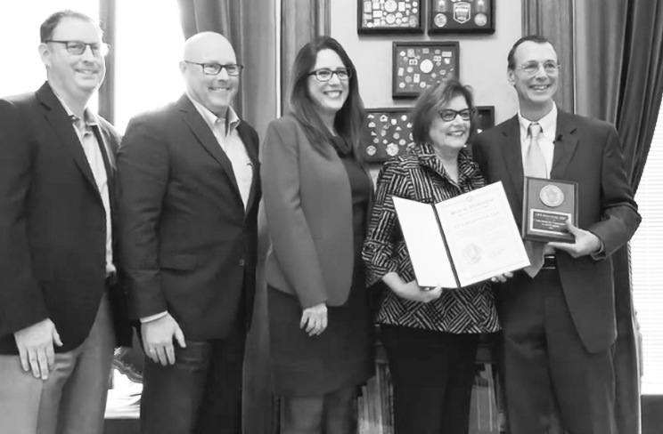 Five people standing together for a photo, one holding an open certificate and another holding the National Association of Secretaries of State Medallion Award plaque.