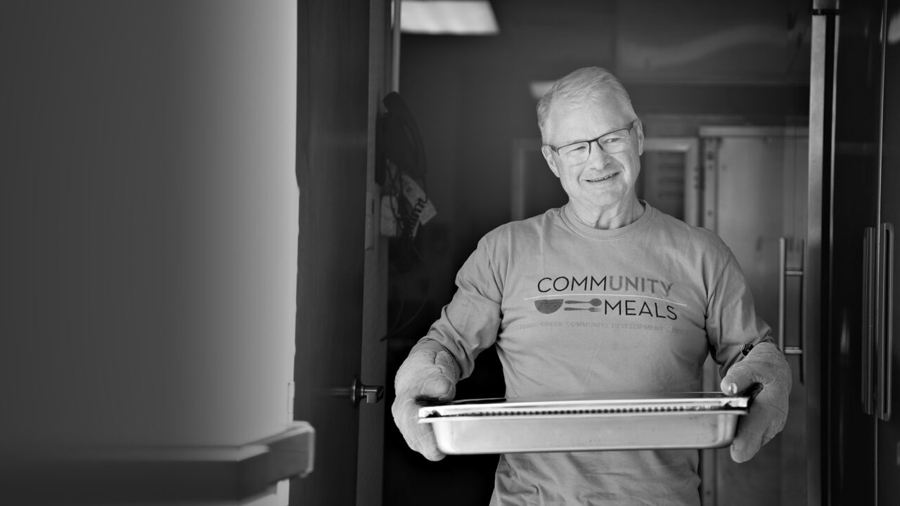 Randy Teuber carries a tray of food through the kitchen door while volunteering at Community Meals.